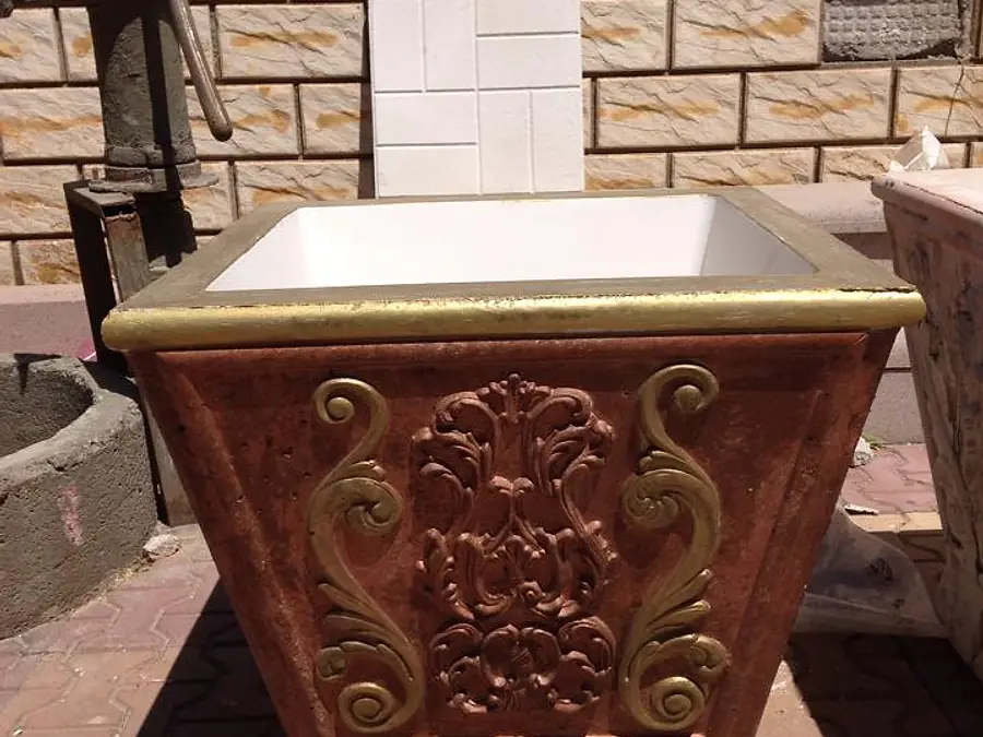 Kabartma desenli, kırmızı ve altın rengine boyanmış konik beton çiçeklik