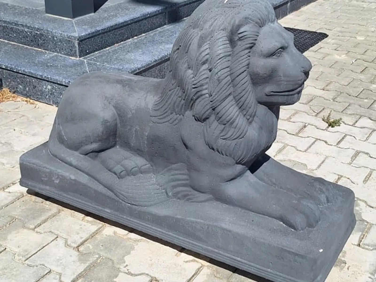 Kaideli beton aslan figürünün tesis girişindeki kilitli parke taşı üzerinde yandan görünümü