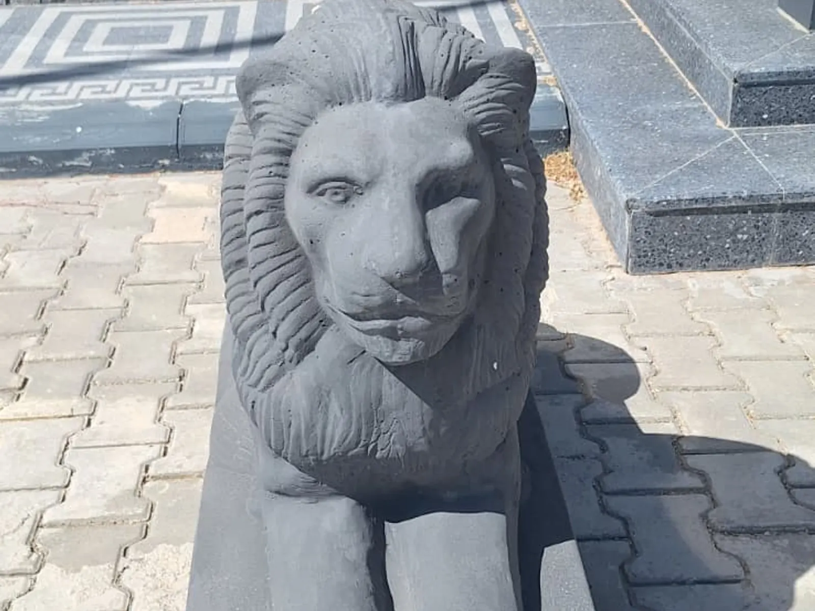 Beton aslan figürünün önden yakın çekimi, arkada taş görünümlü duvar kaplaması